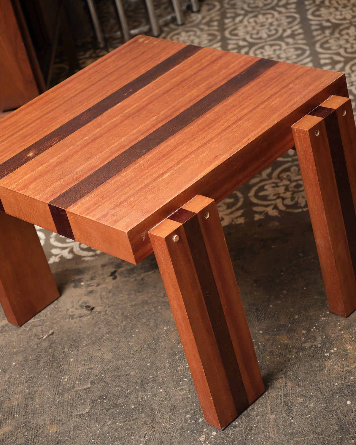 Angled view of the tabletop and legs showing striped inlay and brass pin details.