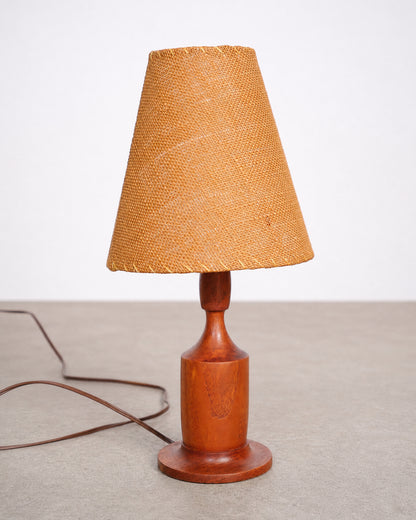 Vintage small walnut lamp with woven wicker shade on a plain background.