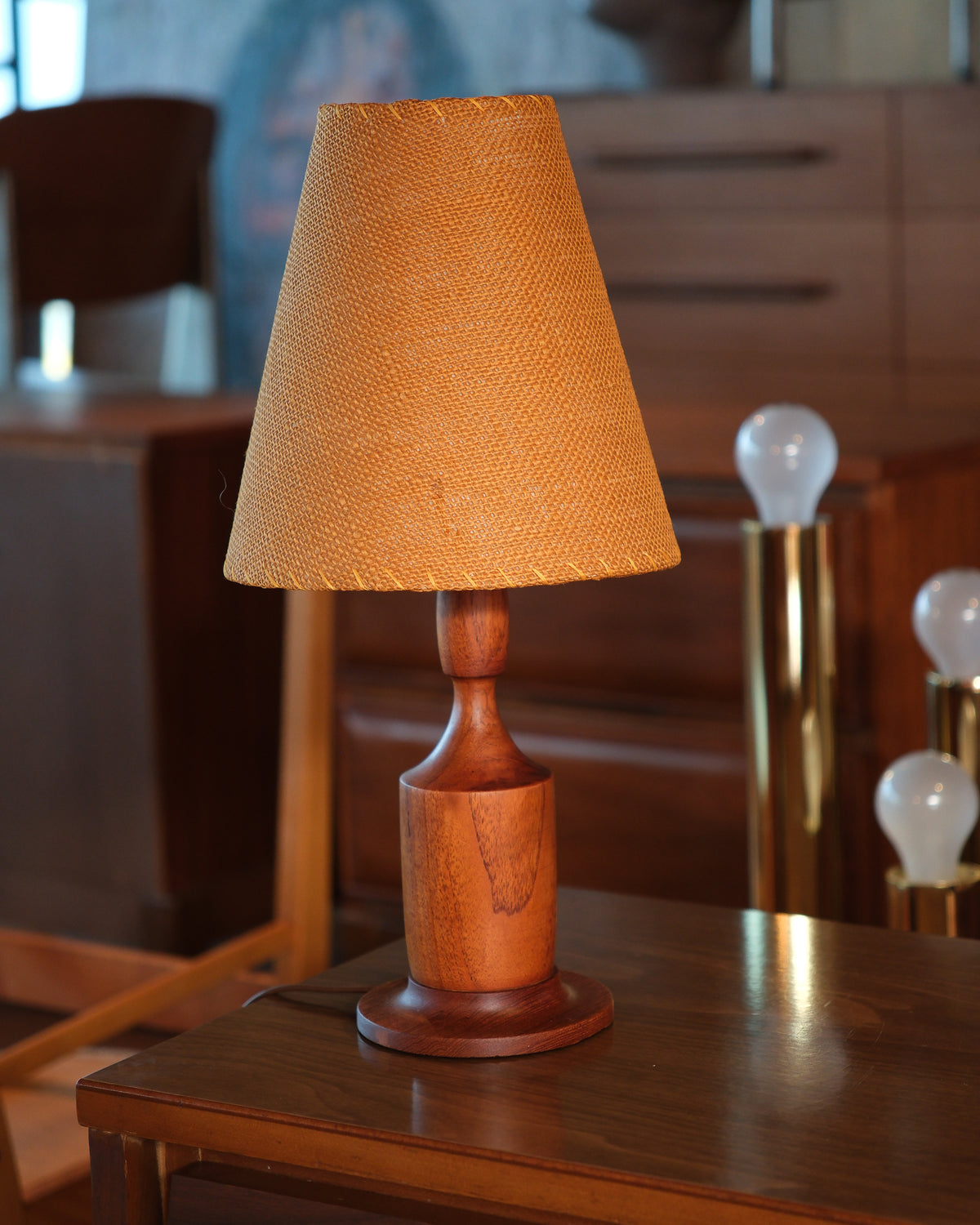 Walnut lamp displayed on a wood side table in a furniture showroom setting.