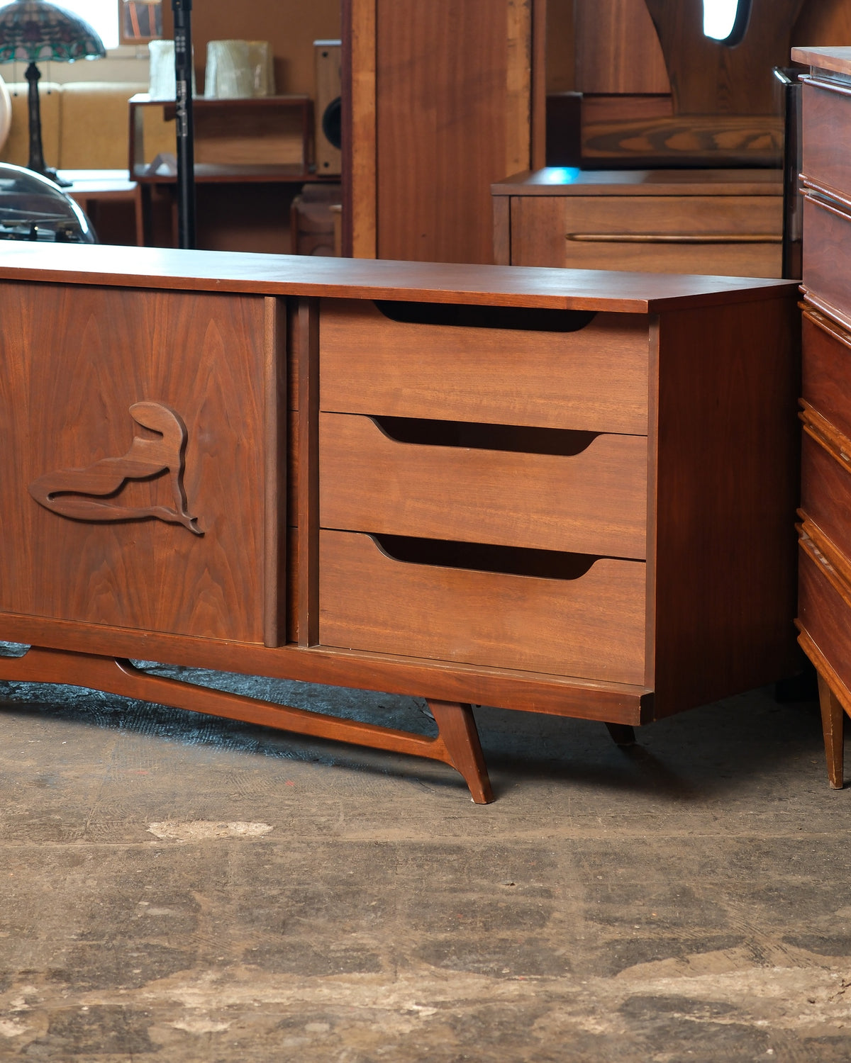 Front corner detail of the sideboard showing three drawers and the carved figural sliding door