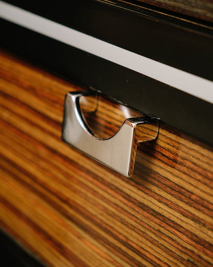 Close-up of a chrome drawer pull against striped zebrawood grain and black-and-white banded trim.