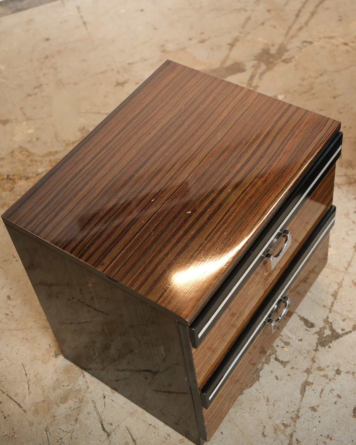 Angled view of a nightstand showing the two-drawer front with chrome hardware and glossy top.