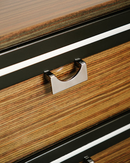 Close-up detail of the chrome pull and black-and-white trim between drawers on zebrawood front.